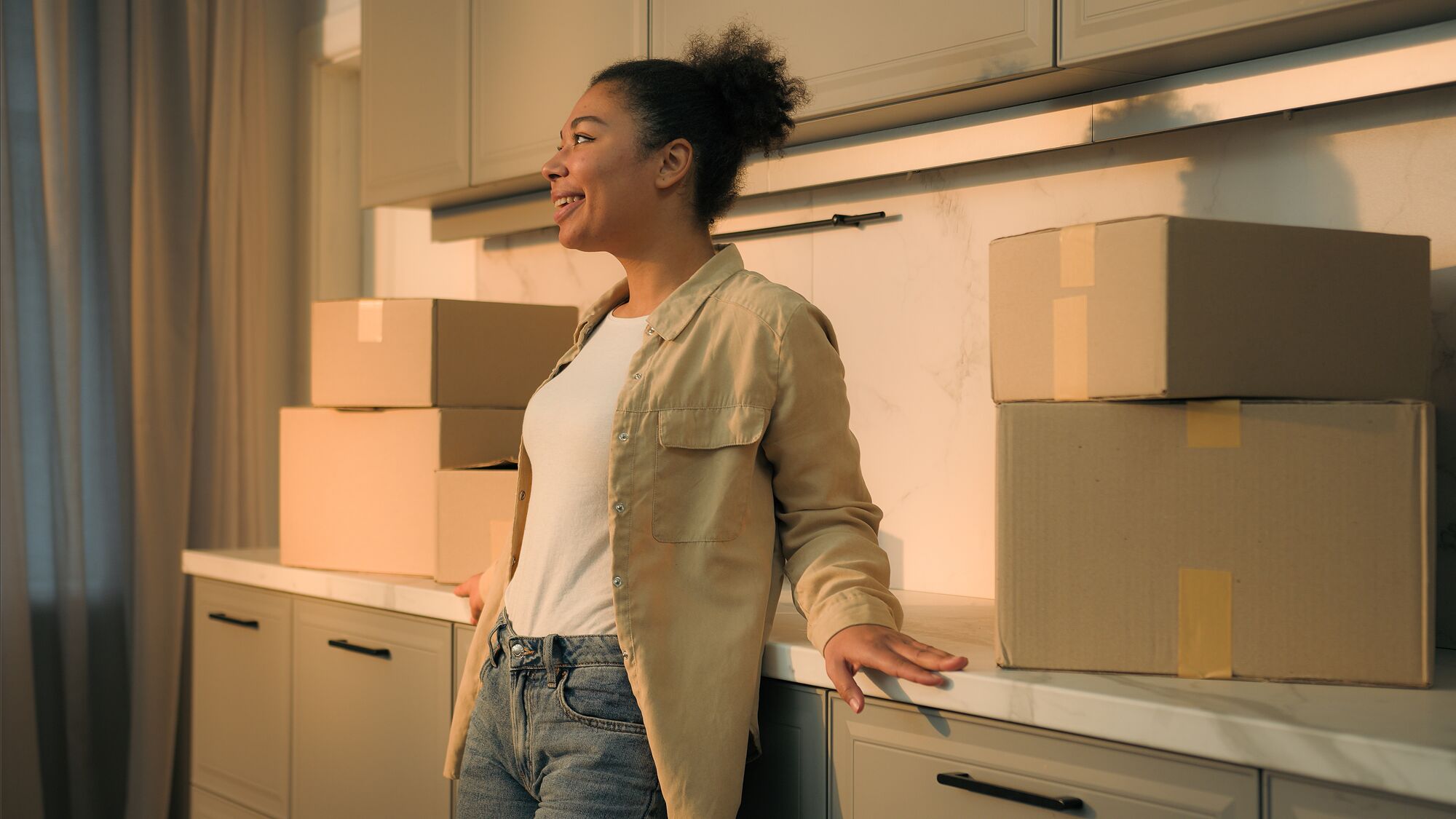 Happy smiling woman African American girl cheerful homeowner renter tenant moving in new own home enjoy modern kitchen renovation packed cardboard boxes relocation day rent buy house credit mortgage